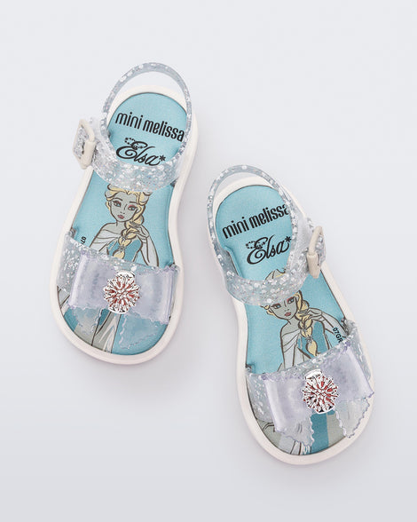 Top view of a pair of glitter clear Mini Melissa Mar Sandal Princess sandals with a snowflake bow detail on the front strap, an ankle strap and Princess Elsa soul