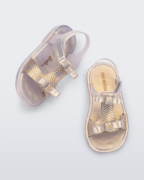 Side and top view of a pair of pearly gold baby Dream Sandal with two bows and gold detail on strap