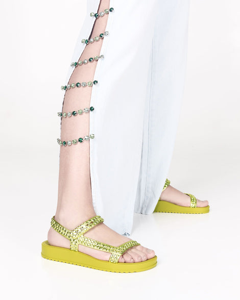 Model's legs in slit pants wearing a pair of green Lust sandals with metallic green strap