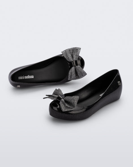 Angled view of a pair of glitter black Ultragirl Sweet kids ballerina flats with bow