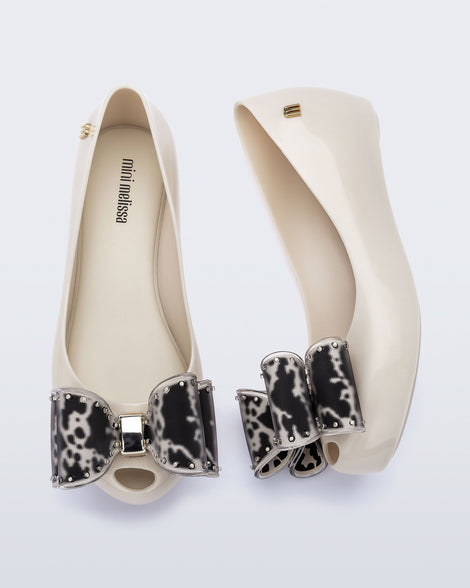 Top and side view of a pair of beige kids Ultragirl Classic Bow kids flats with black and clear bow