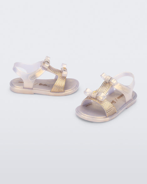 Side and angled view of a pair of pearly gold baby Dream Sandal with two bows and gold detail on strap