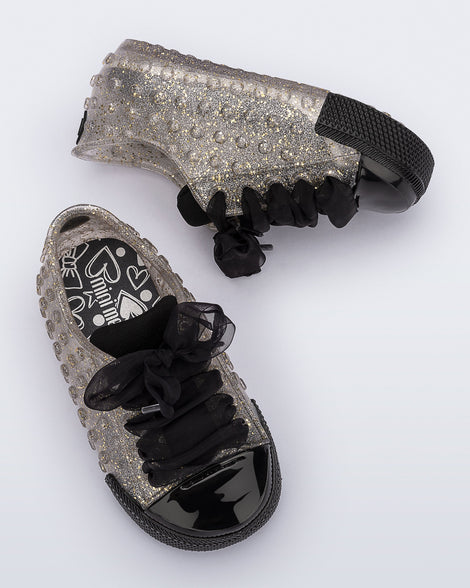 Top and side view of a pair of clear glitter Polibolha baby sneakers with black laces.