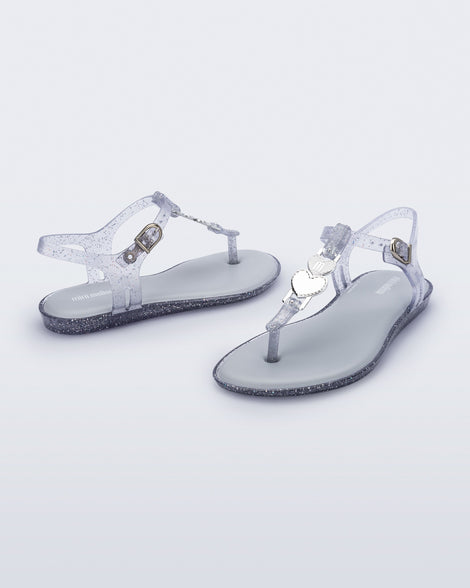 Angled view of a pair of clear glitter Solar kids sandal with a heart embellishment