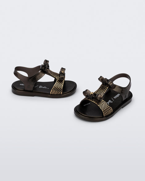 Side and angled view of a pair of black baby Dream Sandal with two bows and gold detail on strap