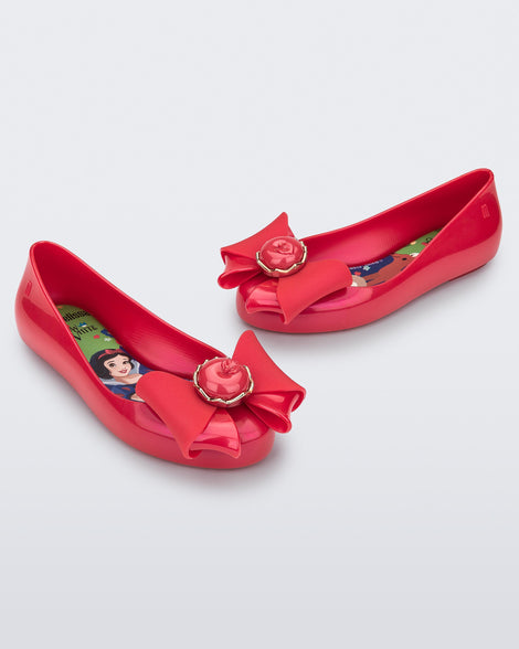 Angled view of a pair of red Sweet Love Snow White kids flats with a red bow with red apple center