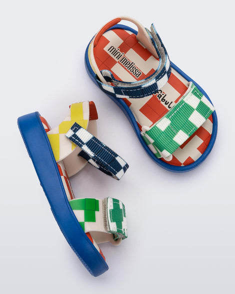 Top and side view of a pair of  blue, yellow, green and beige patterned Mini Melissa Pula Pula + Fabula sandals.