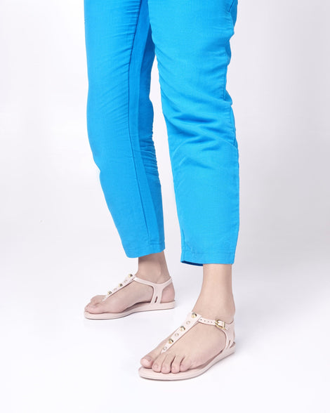 Model's legs in blue pants wearing a pair of pink Melissa Solar studs sandals with gold studded t-strap and gold buckle.