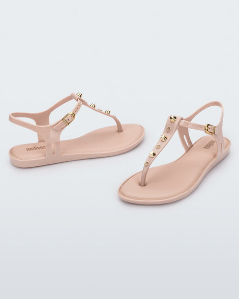 Angled and side view of a pair of pink Melissa Solar studs sandals with gold studded t-strap and gold buckle.