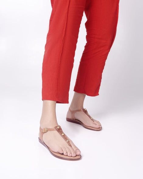 Model's legs in red pants wearing a pair of clear beige Melissa Solar studs sandals with gold studded t-strap and gold buckle.