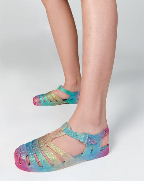 Model's legs wearing a pair of blue and pink glitter Possession sandals.