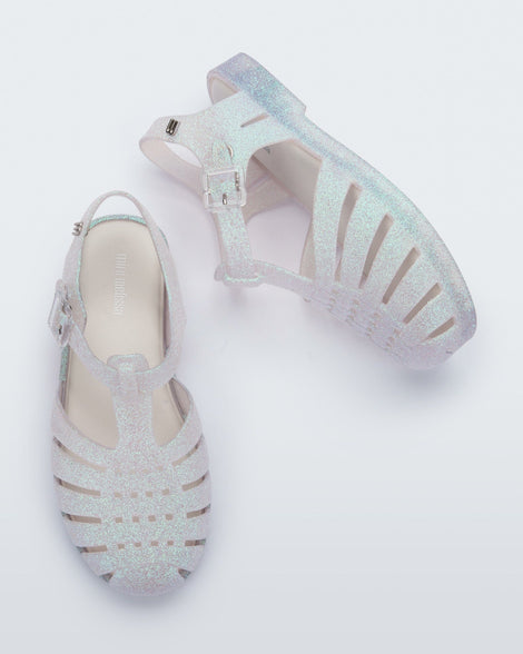 Top and side view of a pair of clear glitter kids Possession sandals.