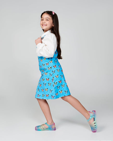 Child model in a blue dress wearing a pair of blue and pink glitter kids Possession sandals.