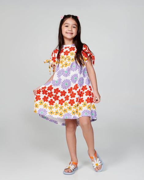 Child model in a floral dress wearing a pair of blue and orange kids Hip Bloom sandal.