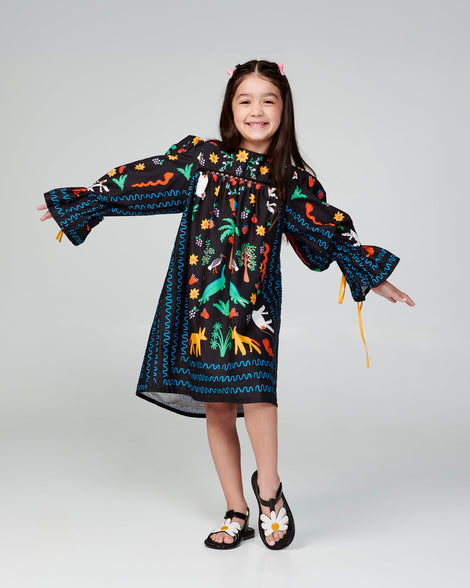 Child model in a black patterned dress wearing a pair of black and white kids Hip Bloom sandal.