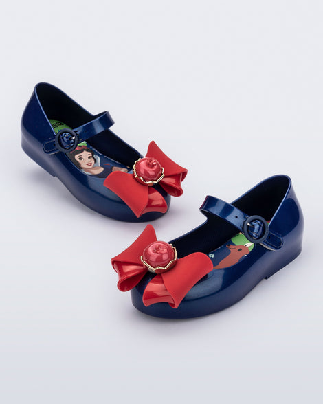 Angled view of a pair of blue Sweet Love Snow White baby flats with a red bow with red apple center