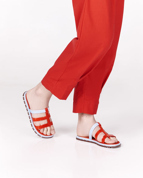 Model's legs wearing a pair of red Path adult sandals with  blue sole