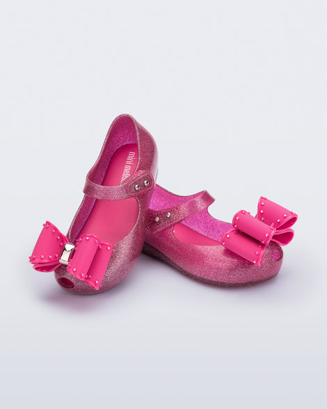 Angled view of a pair of glitter pink baby Ultragirl Classic Bow flats