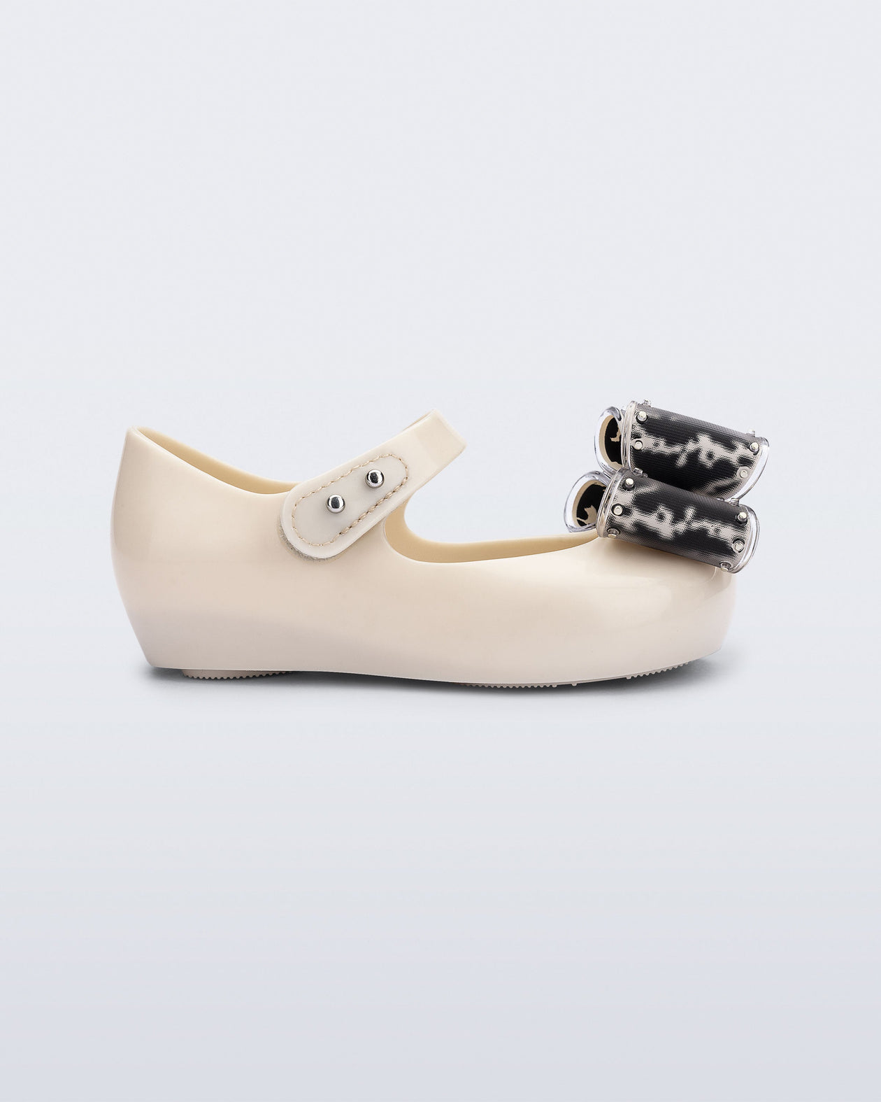 Side view of a beige baby Ultragirl Classic Bow flats with black and clear bow