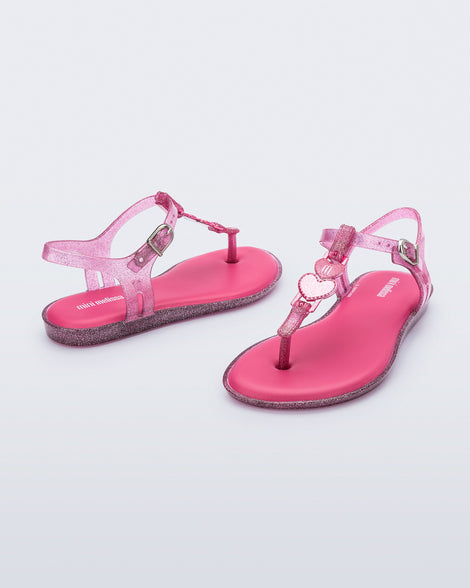 Angled view of a pair of pink glitter Solar kids sandal with a heart embellishment