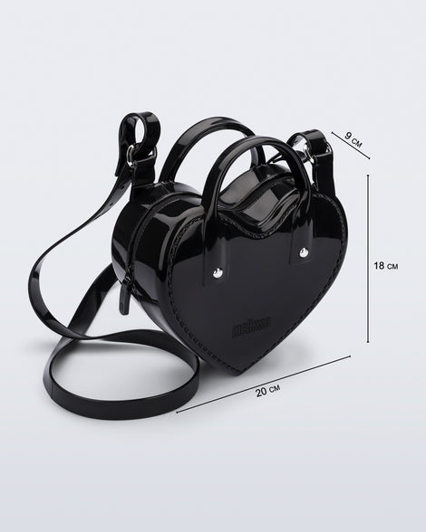 Angled view of a black Heartbeat bag with small handles and longer strap and bag dimensions: 20cm x 9cm x 18 cm.