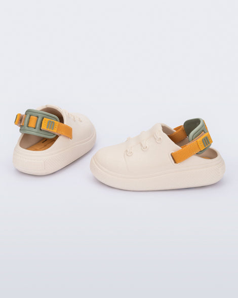 Side and back view of a pair of beige with orange and green back strap Charlie baby sneakers