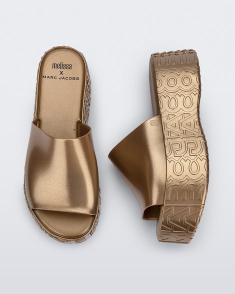 Side and top view of a pair of gold Becky + Marc Jacobs platform slides.