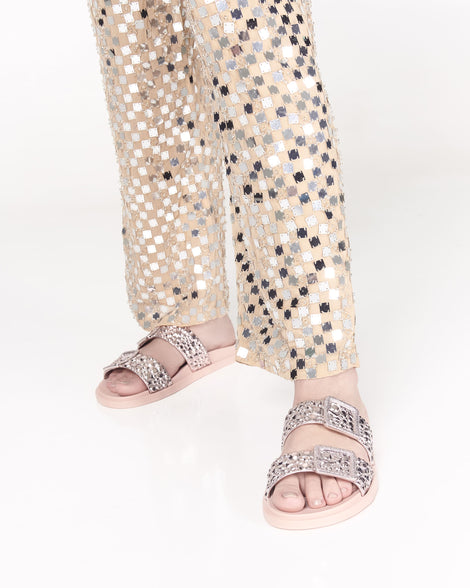 Model's legs in patterned pants wearing a pair of pink Lust slides with metallic buckle straps