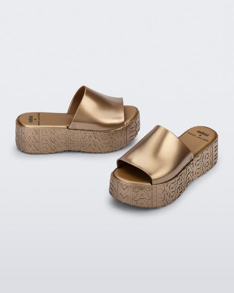 Side and angled view of a pair of gold Becky + Marc Jacobs platform slides.