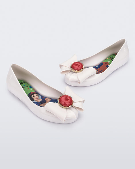 Angled view of a pair of white Sweet Love Snow White kids flats with a white bow with red apple center