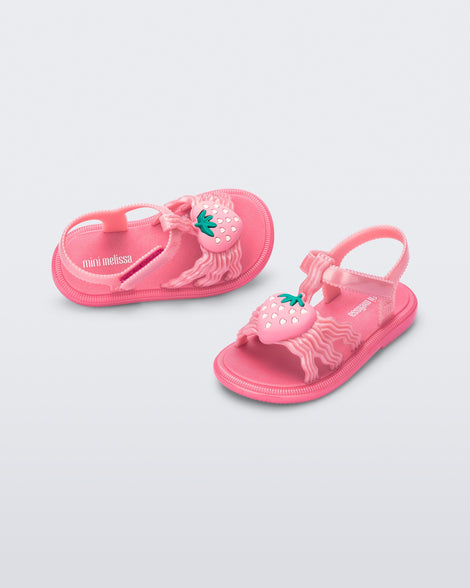 Angled view of a pair of pearly pink baby Hip Sandals with pink strawberry