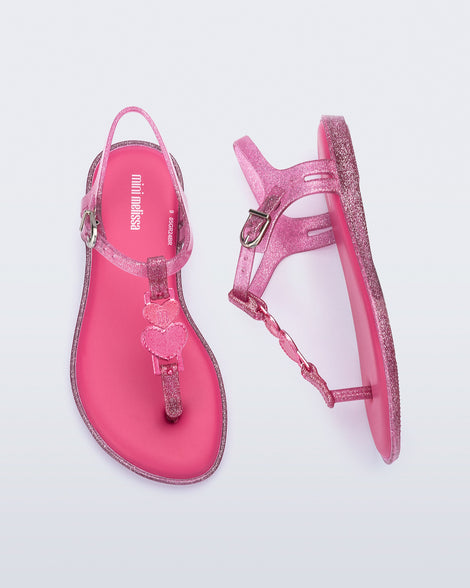 Top and side view of a pair of pink glitter Solar kids sandal with a heart embellishment