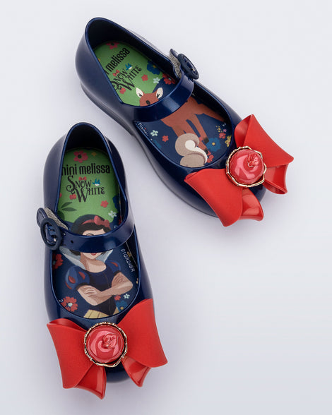 Top view of a pair of blue Sweet Love Snow White baby flats with a red bow with red apple center