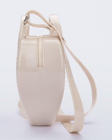 Side view of a beige Heartbeat bag with small handles and longer strap.