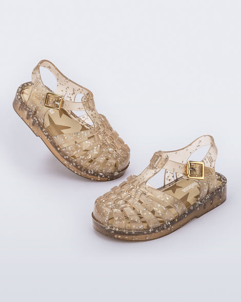 Angled view of a pair of clear beige Possession baby sandals with star glitter