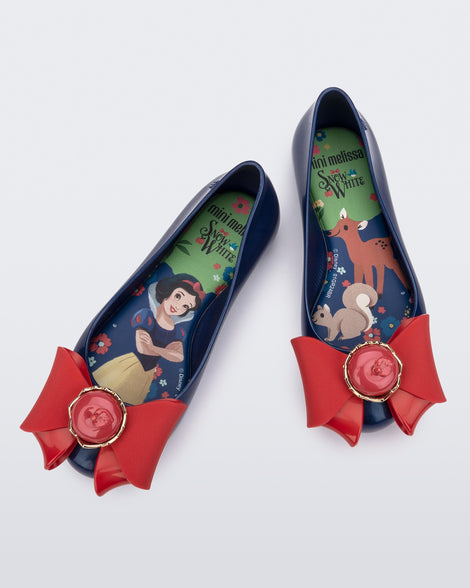 Top view of a pair of blue Sweet Love Snow White kids flats with a red bow with red apple center