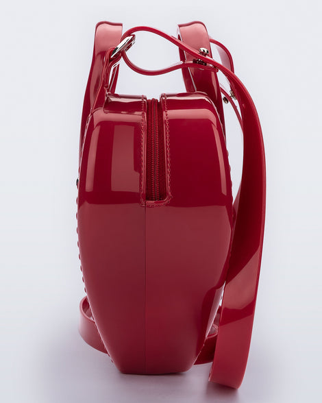 Side view of a red Heartbeat bag with small handles and longer strap.