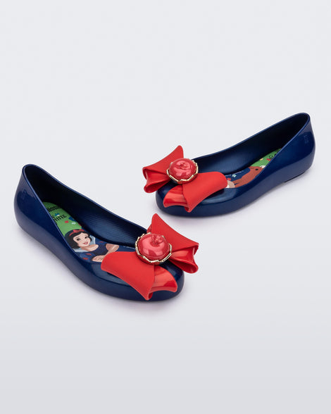 Angled view of a pair of blue Sweet Love Snow White kids flats with a red bow with red apple center