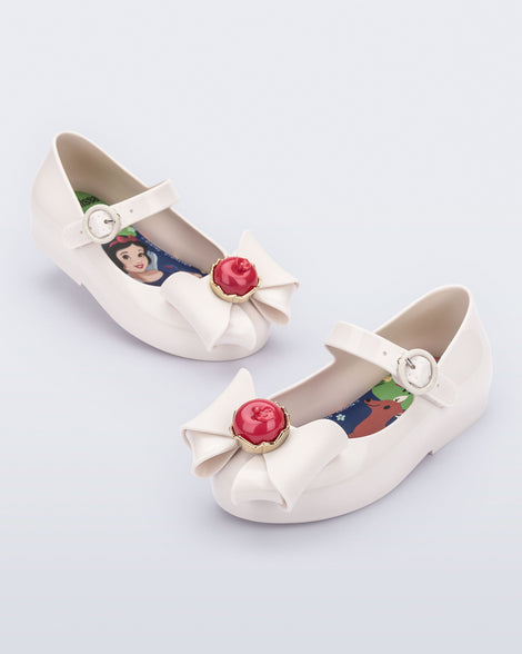 Angled view of a pair of white Sweet Love Snow White baby flats with a white bow with red apple center