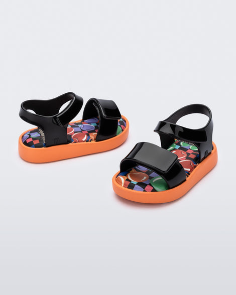 Angled view of a pair of black baby Jump sandals with orange sole