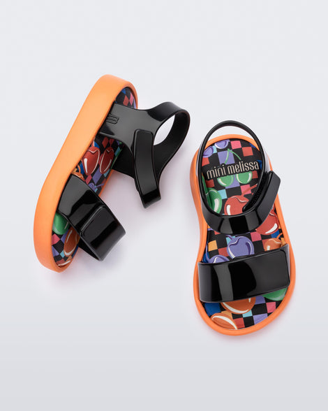 Top and side view of a pair of black baby Jump sandals with orange sole