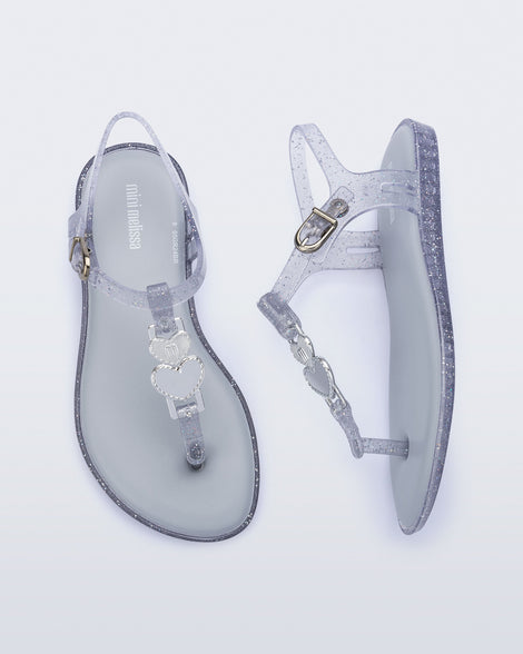 Top and side view of a pair of clear glitter Solar kids sandal with a heart embellishment