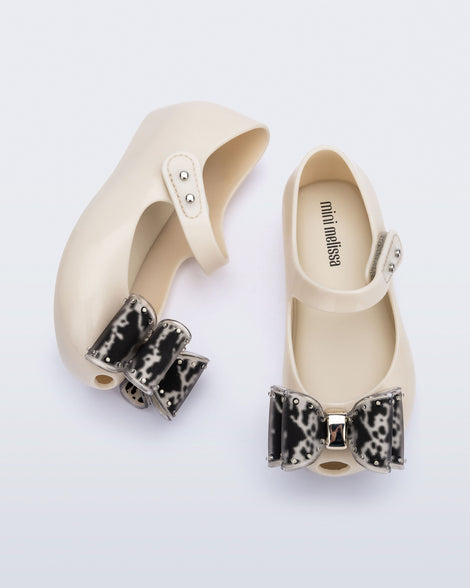 Top and side view of a pair of beige baby Ultragirl Classic Bow flats with black and clear bow