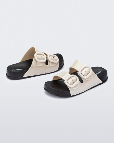 Angled view of a pair of kids beige Cozy slides with black sole