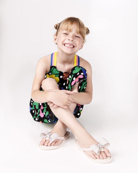 Model posing wearing a pair of Mini Melissa Flip Flops in beige with bow applique