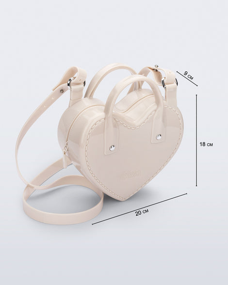 Angled view of a beige Heartbeat bag with small handles and longer strap and bag dimensions: 20cm x 9cm x 18 cm.