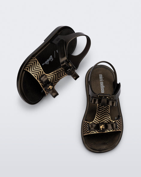 Side and top view of a pair of black baby Dream Sandal with two bows and gold detail on strap