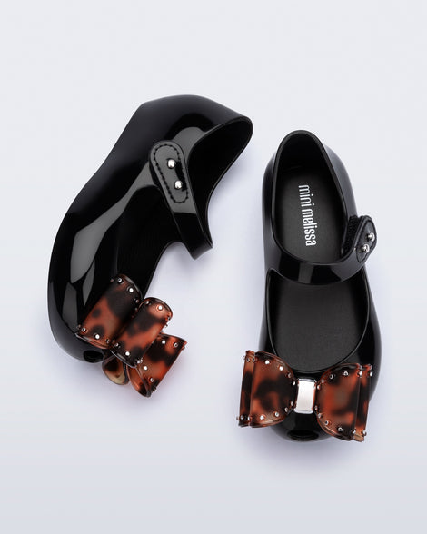 Top and side view of a pair of black baby Ultragirl Classic Bow flats with tortoise bow