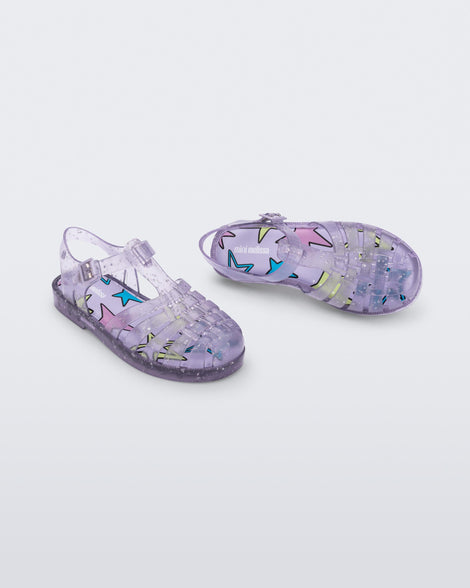 Angled view of a pair of clear lilac Possession kids sandals with star glitter