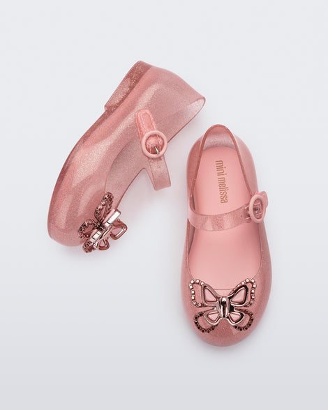 Top view of a pair of glitter pink Mini Melissa Sweet Love Butterfly flats with a top strap and metallic pink butterfly detail on the toe